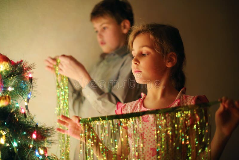 Girl and boy decorated Christmas tree with tinsel at evening stock images Girl and boy decorated Christmas tree with tinsel at evening stock images