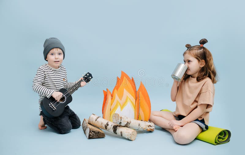 Girl and boy sitting next to fake campfire, acting a scene over blue background