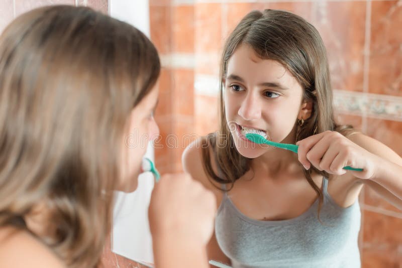 Girl brushing her teeth in front of a mirror