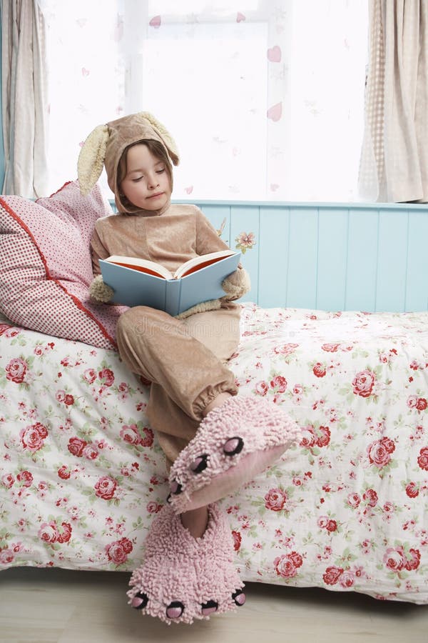 Girl In Bunny Costume And Monster Slippers Reading Book On Bed