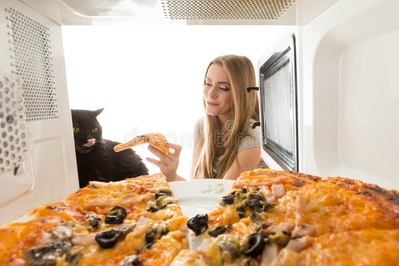 The girl and a cat looking in a microwave