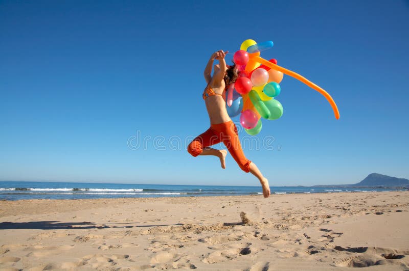 Girl with colorful balloons jumping on the beach