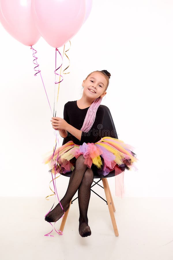 Girl in colorful tutu in the studio with white background during photo shoot with pink balloon. Cute young ballerina