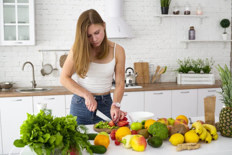 The girl cuts with a knife pepper and tomato.