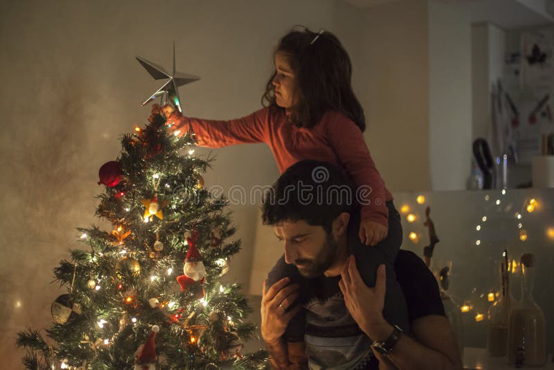 Girl and Dad Setting Up the Christmas Tree with Star, Lights and Stock