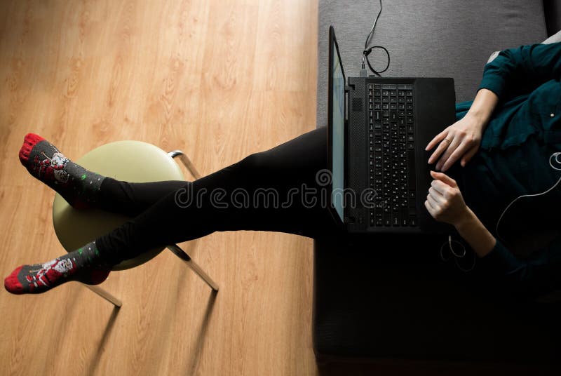 Girl in dark green blouse is sitting on grey couch at home. Working day of freelancer earning money on Internet. Woman is