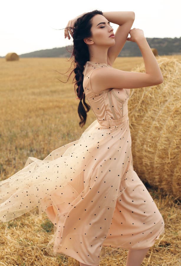 Girl with dark hair in elegant dress posing on the hay