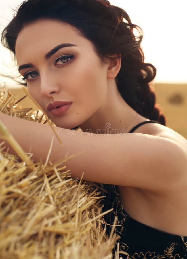 Girl with dark hair in elegant dress posing on the hay