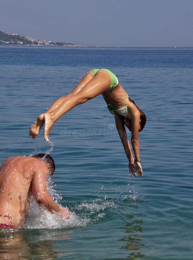 The young girl is jumping (plung in) from his fathers shoulders in Adriatic sea - Croatia (Dalmatia). Vertical color photo. The young girl is jumping (plung in) from his fathers shoulders in Adriatic sea - Croatia (Dalmatia). Vertical color photo.