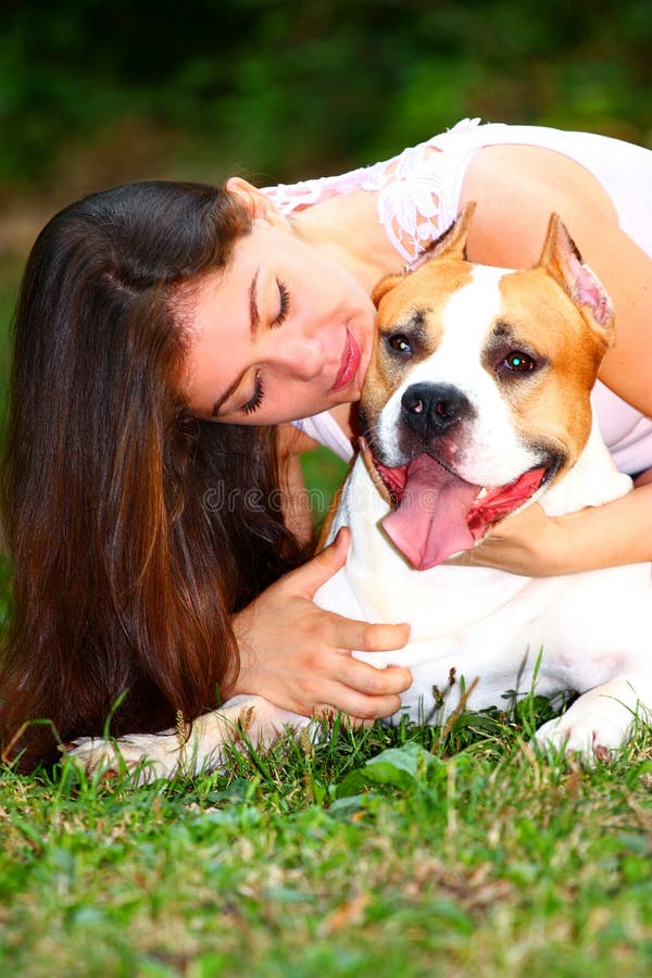 Portrait of a beautiful girl holding , hugging her dog (American Staffordshire Terrier) with her arms out in a park. Portrait of a beautiful girl holding , hugging her dog (American Staffordshire Terrier) with her arms out in a park