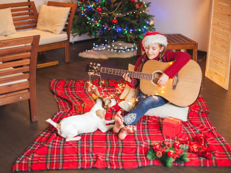 Girl with a dog playing the guitar and singing near christmas tree