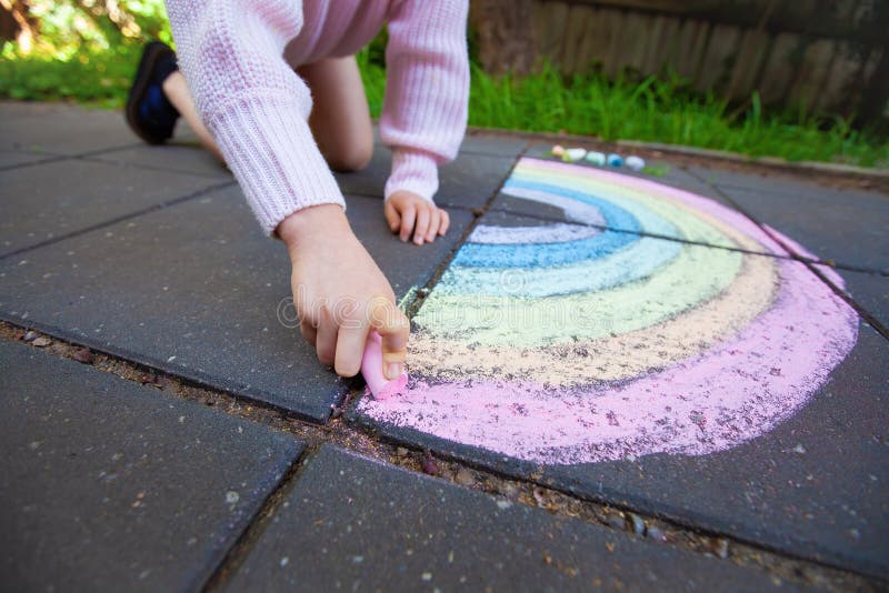 Girl drawing rainbow with chalk on pavement. stock images