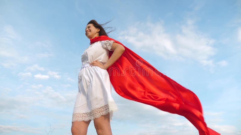 Girl dreams of becoming a superhero. sexy superhero girl standing on the field in a red cloak, cloak fluttering in the royalty free stock photos Girl dreams of becoming a superhero. sexy superhero girl standing on the field in a red cloak, cloak fluttering in the royalty free stock photos