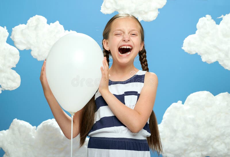 Girl dressed in striped dress posing on a blue background with cotton clouds, the concept of summer and happiness