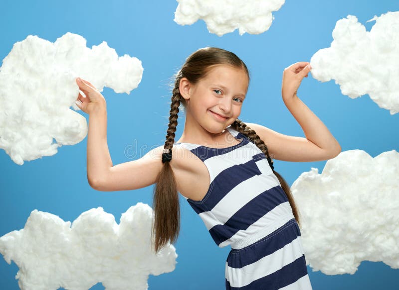 Girl dressed in striped dress posing on a blue background with cotton clouds, the concept of summer, holiday and happiness