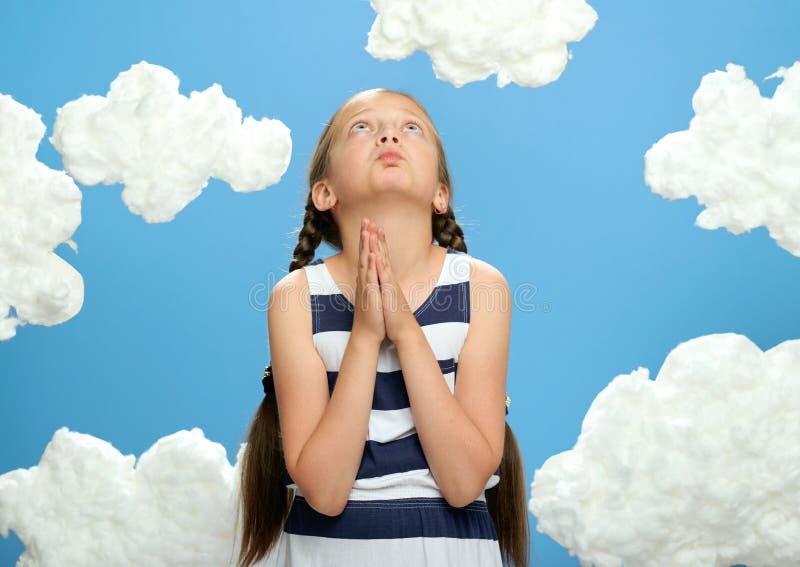 Girl dressed in striped dress posing on a blue background with cotton clouds, looking up and dreaming, prays, the concept of summe