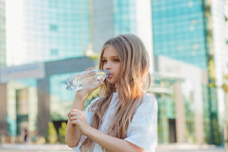 Beautiful teen girl holding bottle of water, smiling and drinking fresh  water Stock Photo