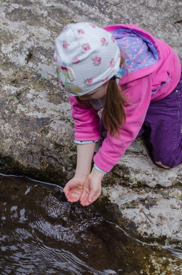 Girl drinks from a mountain stream in early spring