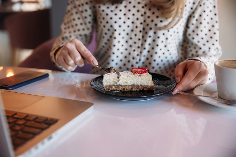Girl eating cake in a cafe. Blonde girl in polka-dot shirt with laptop. Drinking cappuccino. Business lady royalty free stock photography Girl eating cake in a cafe. Blonde girl in polka-dot shirt with laptop. Drinking cappuccino. Business lady royalty free stock photography