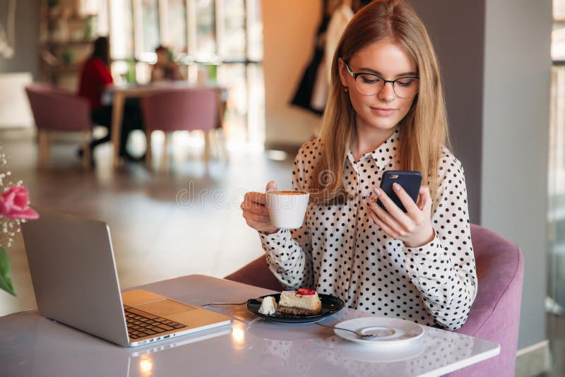 Girl eating cake in a cafe. Blonde girl in polka-dot shirt with laptop. Drinking cappuccino. Business lady royalty free stock images Girl eating cake in a cafe. Blonde girl in polka-dot shirt with laptop. Drinking cappuccino. Business lady royalty free stock images