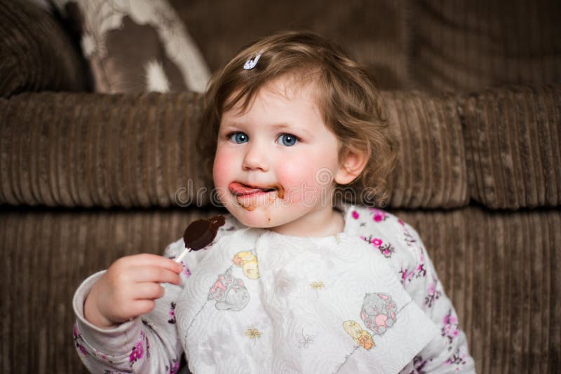 Girl (3) eating chocolate lollipop with chocolate on her face