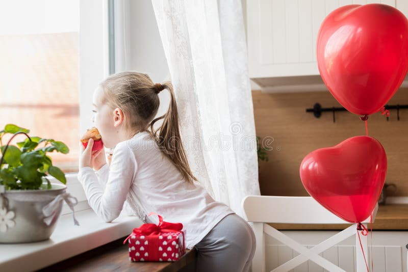 Girl eating her birthday cupcake in the kitchen, surrounded by balloons. stock photo Girl eating her birthday cupcake in the kitchen, surrounded by balloons. stock photo