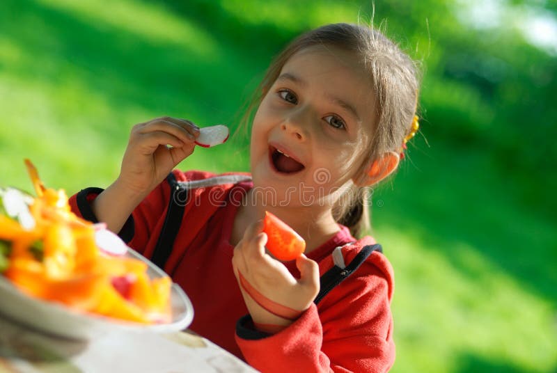 The girl eats a tomato and a garden radish