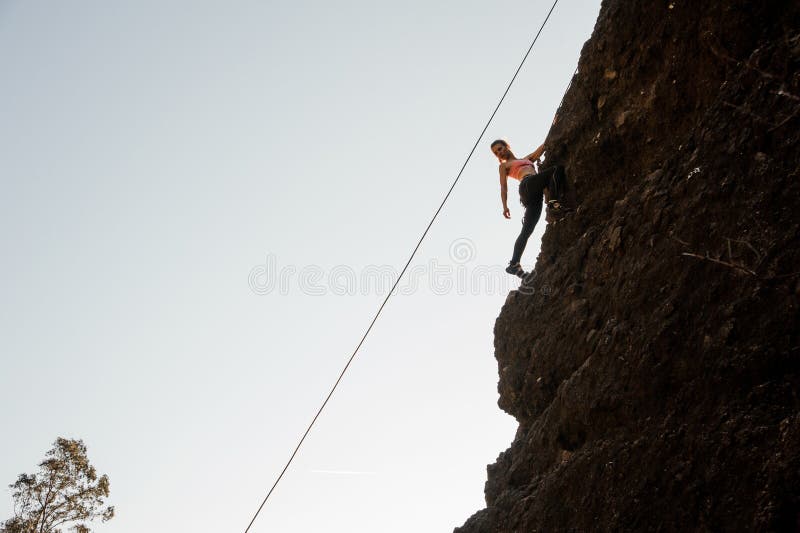 Girl equipped with a rope climbing on the sloping rock and looking down royalty free stock image Girl equipped with a rope climbing on the sloping rock and looking down royalty free stock image