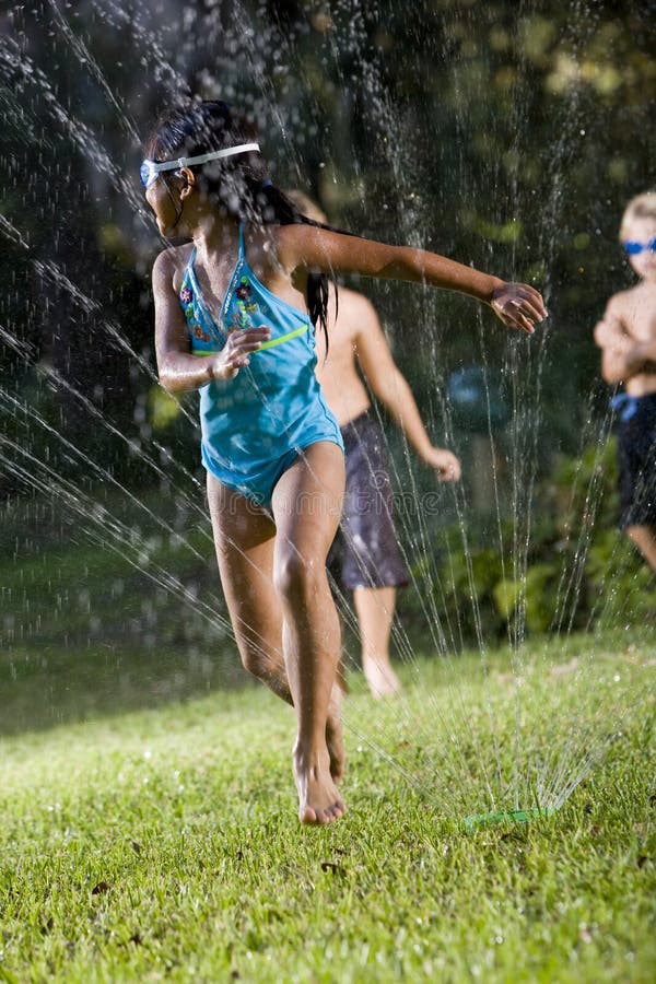 Girl with friends playing in lawn sprinkler