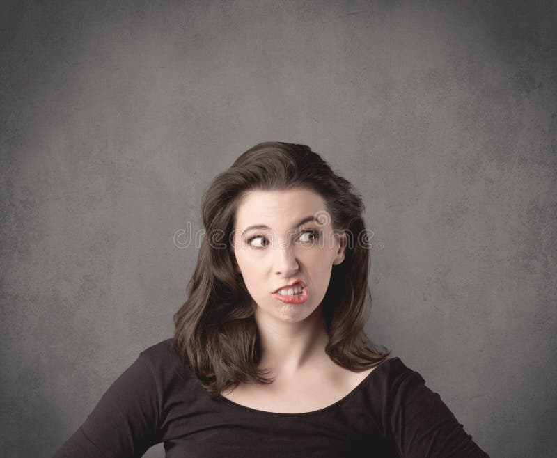 A pretty young teenage girl standing in front of a grey clear empty urban wall background concept while making funny faces. A pretty young teenage girl standing in front of a grey clear empty urban wall background concept while making funny faces.