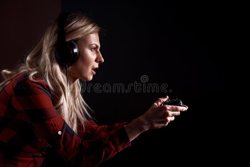 Girl gamer in headphones and with a joystick enthusiastically playing on the console