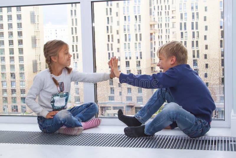 The girl gives five to the boy. children sit on the floor by the window in the new house. Photo of children&x27;s leisure house.