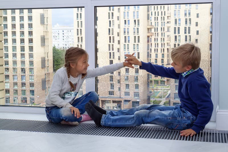 Girl gives five to boy. children sit on floor by window in new house during quarantine. Photo of children leisure house. Brother