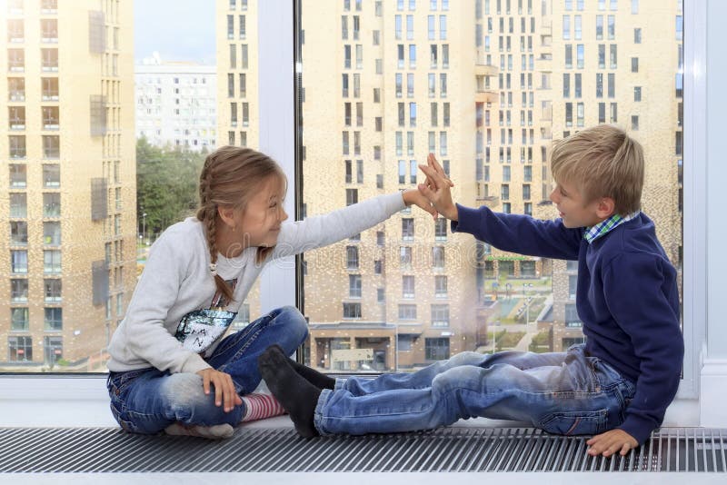 Girl gives five to boy. children sit on floor by window in new house during quarantine. Photo of children leisure house. Brother