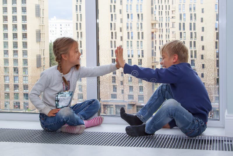 Girl gives five to boy. children sit on the floor by window in new house during quarantine