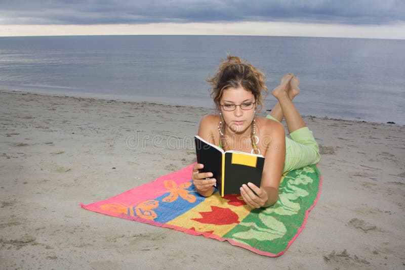 Girl with glasses reading a book in the beach