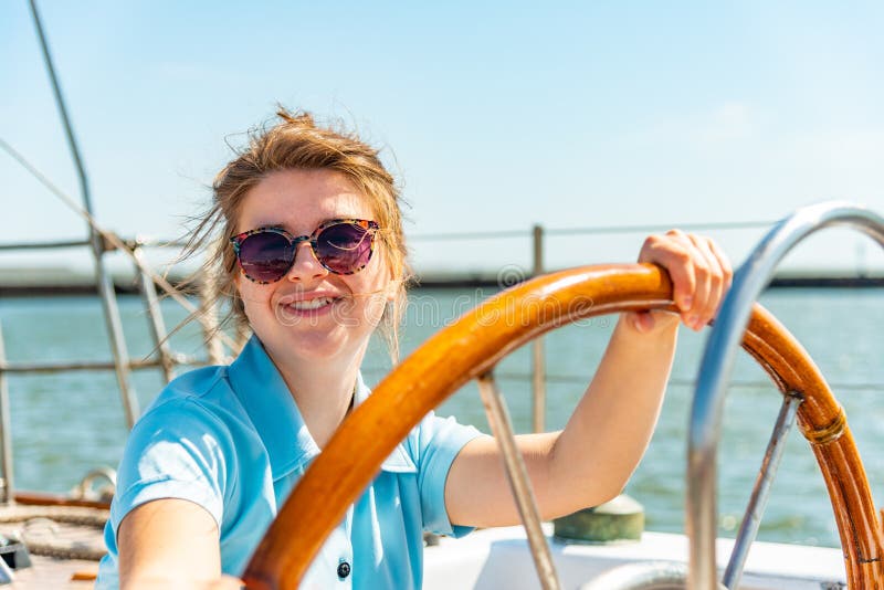 A Girl In Glasses Sits Near The Wheel Next To On The Deck Of A Yacht 