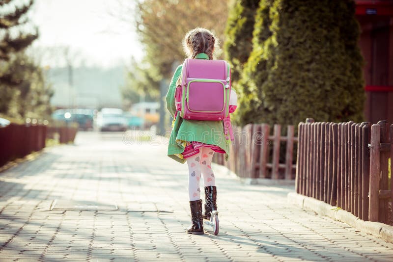 Girl goes to school on a scooter. back view