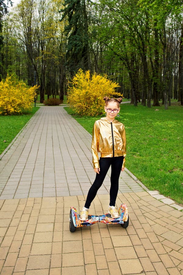A girl in a gold jacket stands on self balancing scooter in the park stock image A girl in a gold jacket stands on self balancing scooter in the park stock image