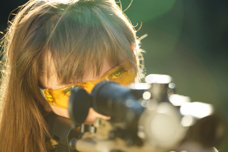 A young girl with a gun for trap shooting and shooting glasses aiming at a target