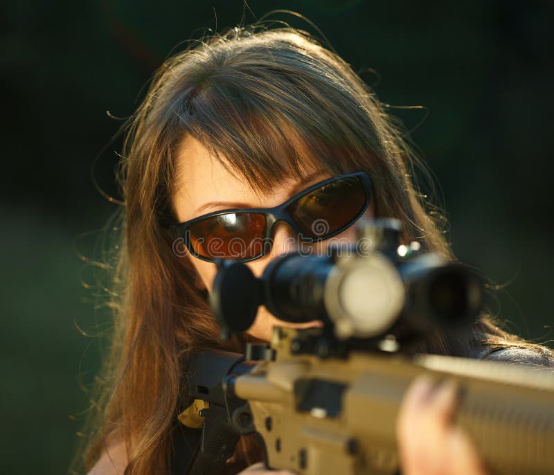 A young girl with a gun for trap shooting and shooting glasses aiming at a target