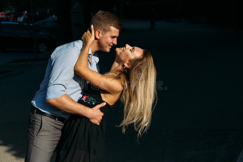 The girl and the guy are smiling, bending over, the guy wants to kiss the girl. the sun shines on their faces. pair on a dark