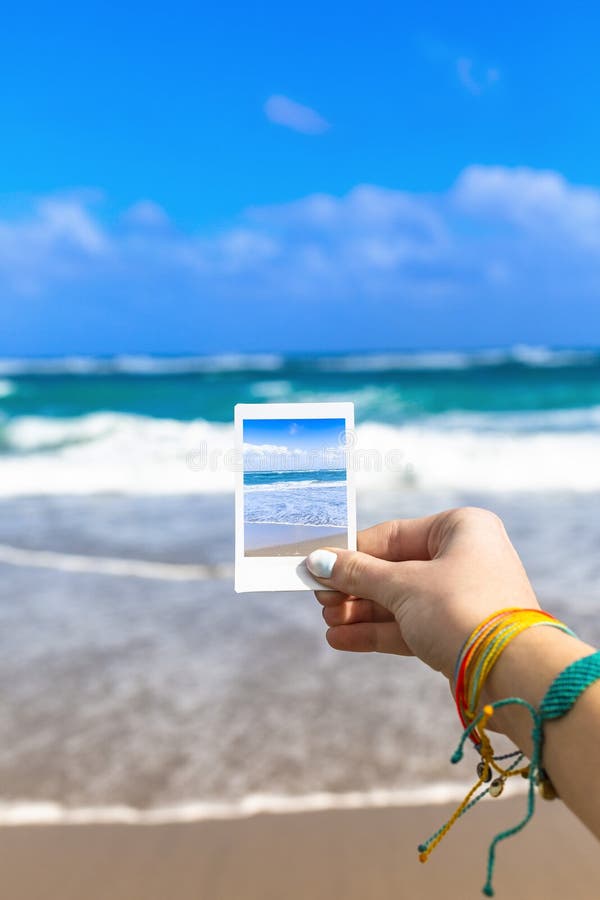 Girl Hand Holding Instant Photo Of Sea Beach Landscape, focus on hand and photo