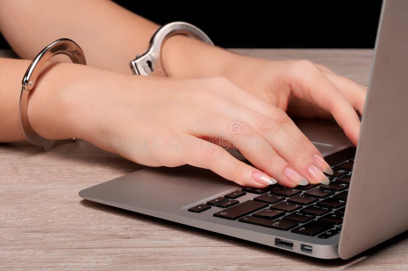 A girl in handcuffs is working on a laptop. The concept of censorship or restriction of freedom of speech. Very close-up