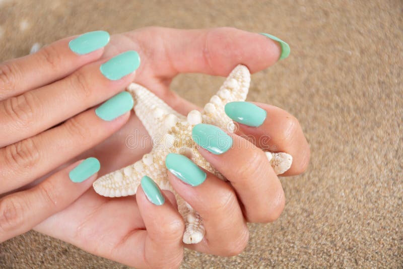 Girl hands with a turquoise color nails polish holding starfish and sea sand in the background