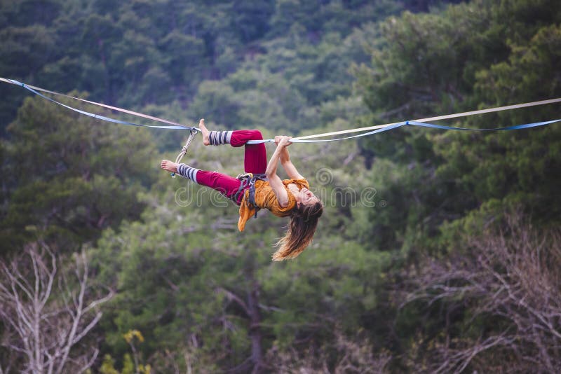 A woman catches balance on the line. Performance athlete in the passage of the sling at high altitude. Exercise in nature. Danger and insurance. The girl is hanging on the line. Trying to get up