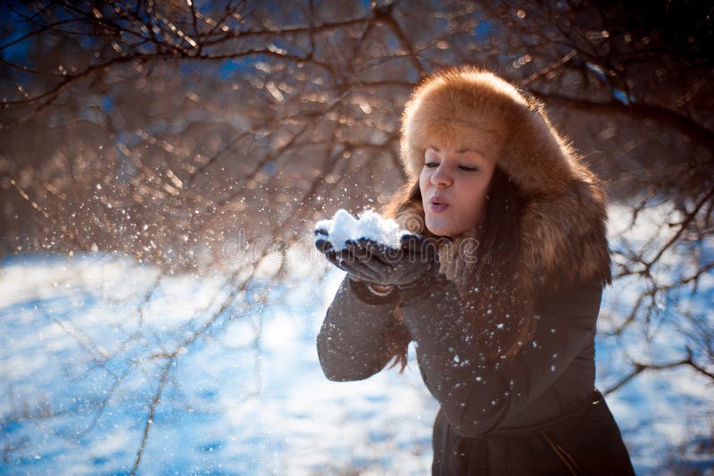Girl in Hat with Ear Flaps Blowing on the Snow. Stock Image - Image of ...