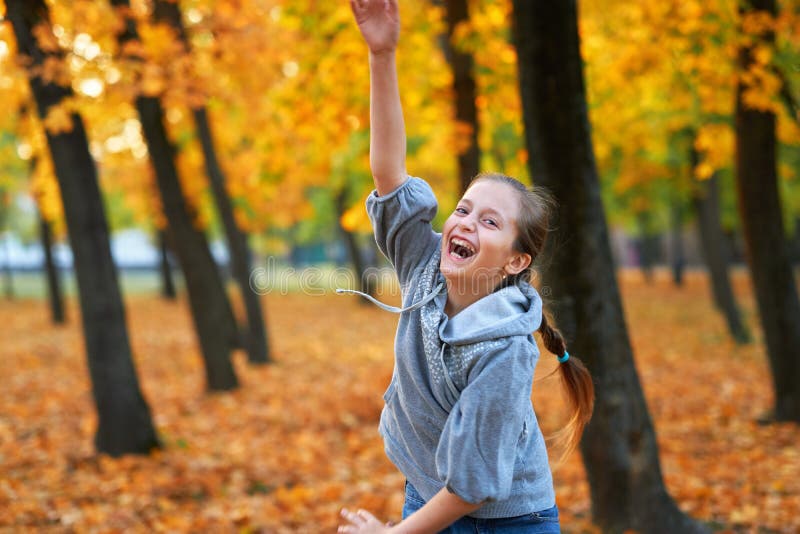 Girl having holiday in autumn city park, running, smiling, playing and having fun. Bright yellow trees and leaves