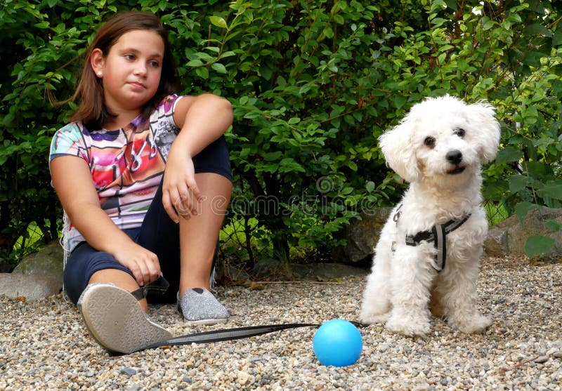 Ragazza e il suo cane che guarda curiosamente in giardino con una palla.