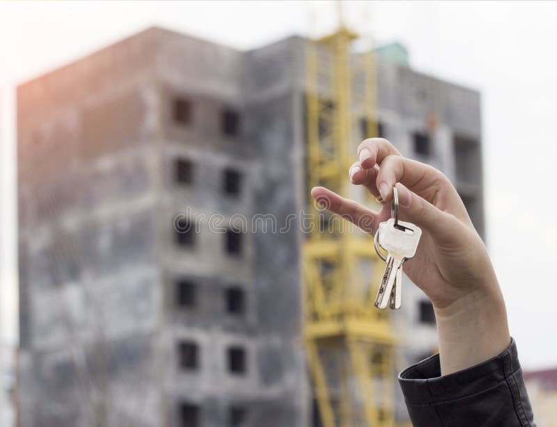 A girl in her hand holds the keys to an apartment on the background of a built house mortgage stock image